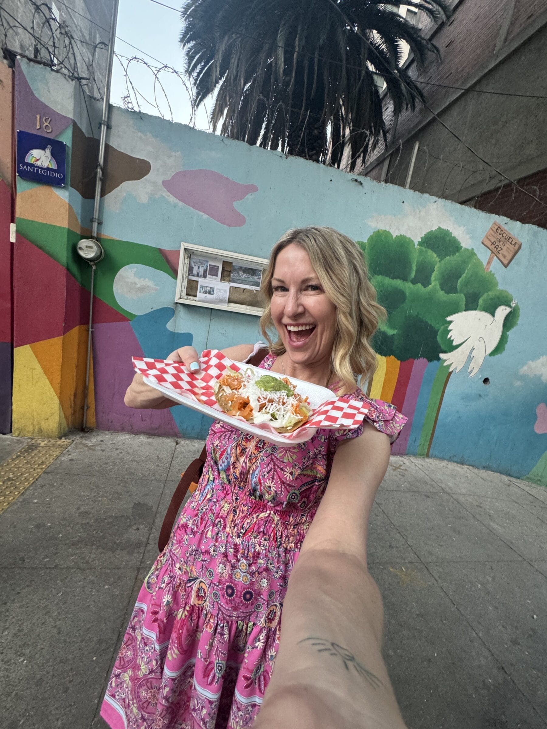 woman in pink dress holds tostada in Mexico City by a mural wall