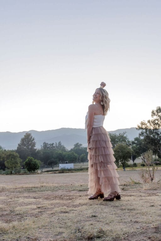 Woman standing in edge of field in Oaxaca, Mexico in a tulle skirt with one hand in air