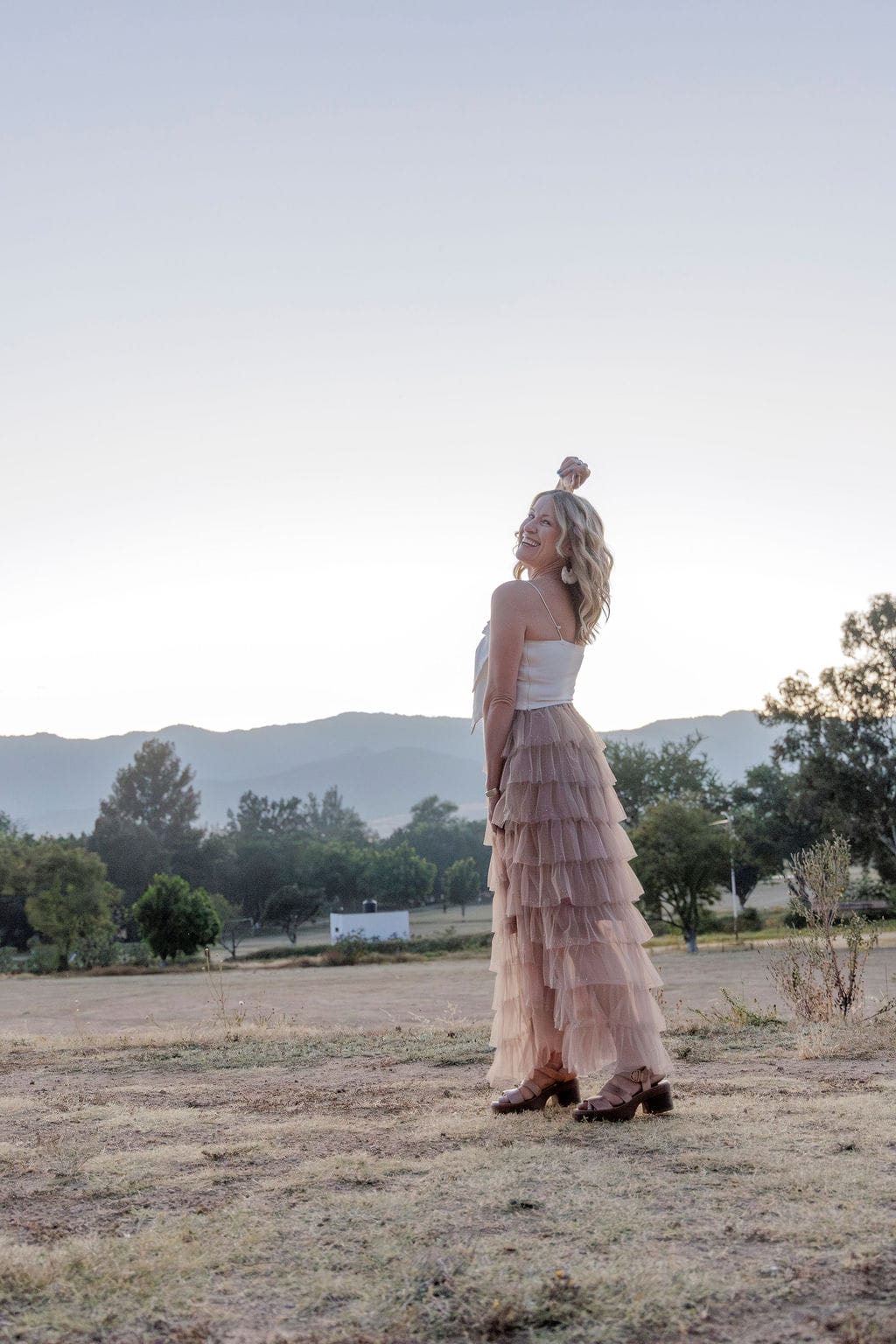 Woman standing in edge of field in Oaxaca, Mexico in a tulle skirt with one hand in air